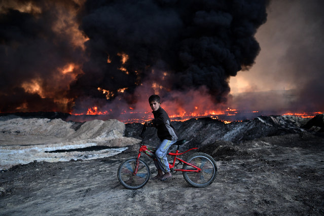 A boy pauses on his bike as he passes an oil field that was set on fire by retreating ISIS fighters ahead of the Mosul offensive, on October 21, 2016 in Qayyarah, Iraq. Several hundred Iraqi families have been made to leave their homes for Mosul by Islamic State fighters as the UN warns they could be used as human shields. ISIS have attacked Kirkuk today as Kurdish and Iraqi forces, backed by a coalition including Britain and the U.S.A continue their offensive to retake Iraq's second largest city of Mosul. (Photo by Carl Court/Getty Images)