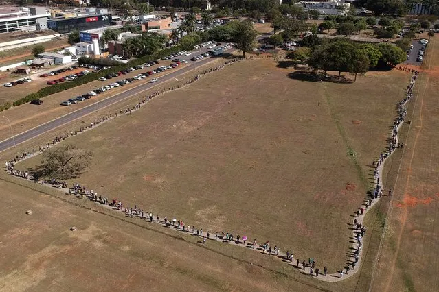 A line of people snakes around a field to enter a COVID-19 vaccination site, as people over age 30 became eligible for a vaccine in Brasilia, Brazil, Tuesday, August 3, 2021. (Photo by Eraldo Peres/AP Photo)