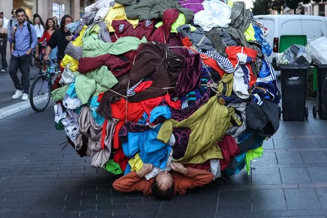 Actor and director Dorian Chavez (C) pushes a ball covered by clothes on the stairs of a metro station as part of a performance called “Sisypolia” denouncing the “absurdity” of overconsumption in Toulouse, southwestern France, on October 5, 2022, as part of the “Biennale des arts vivants de Toulouse”. The performance is inspired by the myth of Sisyphus. (Photo by Charly Triballeau/AFP Photo)