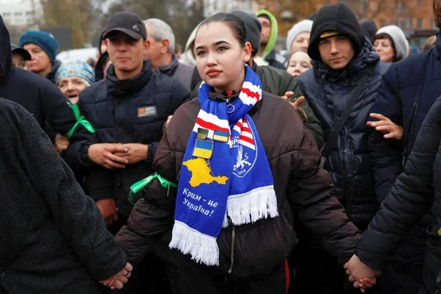 A woman wears a scarf with “Crimea is Ukraine” slogan printed on it, as people wait in line for food distribution after Russia's retreat from Kherson, Ukraine on November 17, 2022. (Photo by Murad Sezer/Reuters)