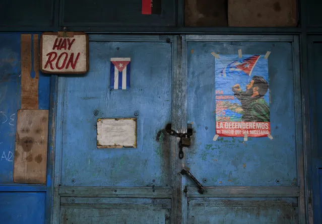A Cuban flag and a poster of Cuba's former president Fidel Castro is seen at the door at a state market in Havana March 18, 2016. The words read, “There is rum”. (Photo by Enrique De La Osa/Reuters)