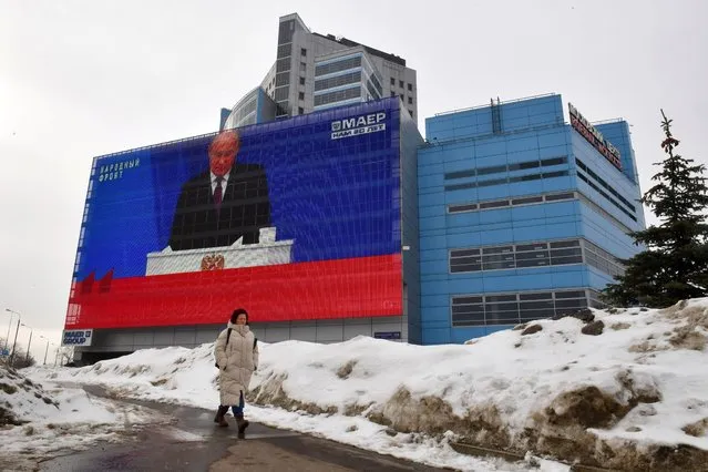 A woman walks past a screen displaying a broadcasting of Russia's President Vladimir Putin's annual state of the nation address on the facade of a building in Moscow on February 29, 2024. (Photo by Olga Maltseva/AFP Photo)