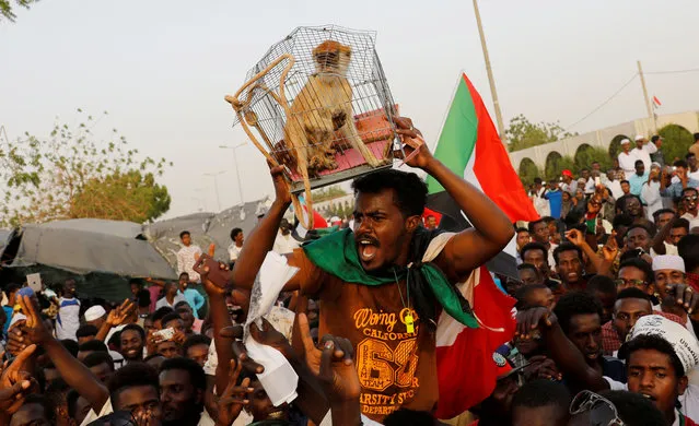A Sudanese protester holds a monkey, that represents former Sudanese President Omar al-Bashir, in a cage wrapped by ropeas he demands capital punishment for him, during a demonstration in front of the Defence Ministry in Khartoum, Sudan, April 19, 2019. (Photo by Umit Bektas/Reuters)