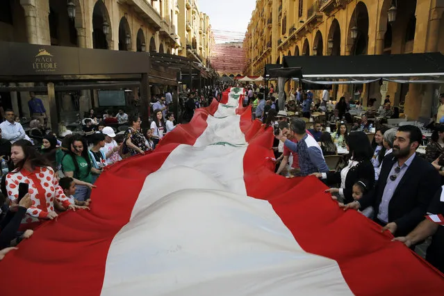 People carry a 300-meter-long Lebanese flag, part of a campaign to break a Guinness World Record, in downtown Beirut, Lebanon, Sunday, April 28, 2019. Beirut Alive, broke the record for the most national flags displayed in one city in 24 hours by hanging 44,000 Lebanese flags in Beirut. (Photo by Bilal Hussein/AP Photo)