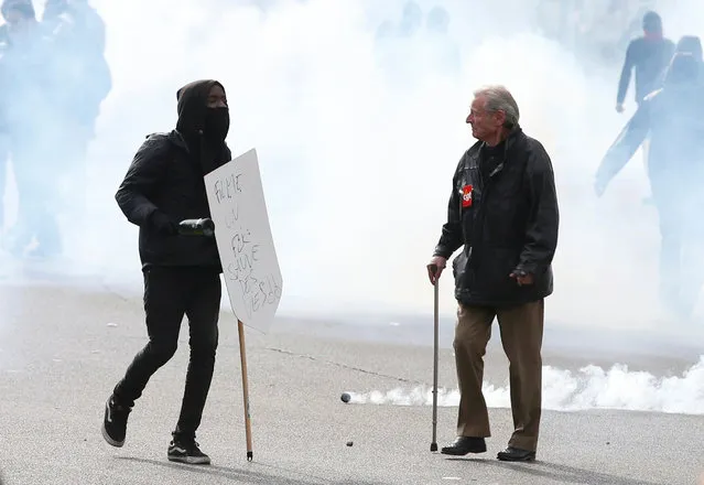 A masked youth and a demonstrator wearing a CGT badge walk through a cloud of tear gas during a demonstration against the French labour law proposal in Paris, France, as part of a nationwide labor reform protests and strikes, April 28, 2016. (Photo by Charles Platiau/Reuters)