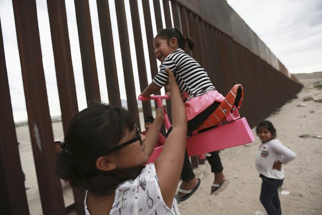 A woman with her little girls helps them play seesaw installed between the border fence that divides Mexico from the United States in Ciudad de Juarez, Mexico, Sunday, July 28, 2019. The author of this seesaw is Ronaldo Rael, a professor of architecture in California. (Photo by Christian Torres/AP Photo)