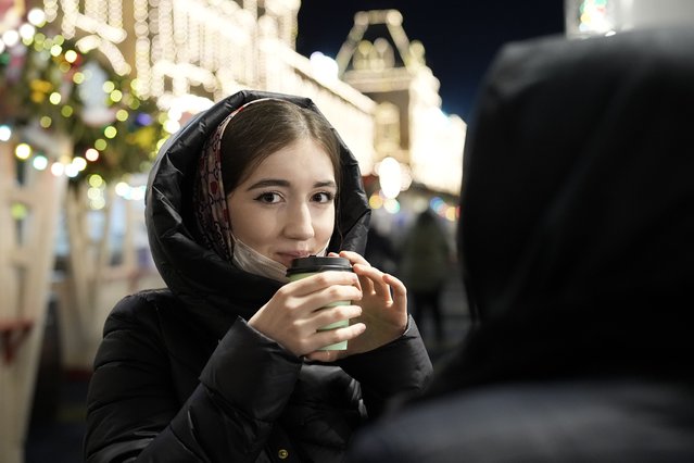 A young woman holds a hot coffee standing at the GUM department store in Moscow, Russia, late Monday, February 14, 2022. (Photo by Alexander Zemlianichenko/AP Photo)