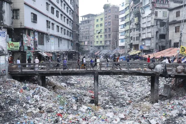 People walk along a bridge over a polluted area in Dhaka, Bangladesh, January 24, 2022. (Photo by Kazi Salahuddin Razu/NurPhoto via Getty Images)