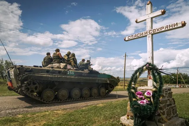 Russia-backed separatist APC rides by an Orthodox cross with a sign reading Save and Guard, with a memorial to the victims of the Malaysian Airlines MH17 plane crash, in the back, near the village of Hrabove, eastern Ukraine, Thursday, July 16, 2015. (Photo by Mstyslav Chernov/AP Photo)