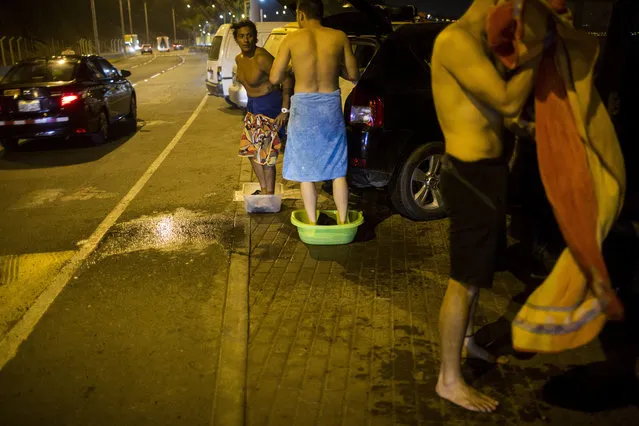 In this March 1, 2017 photo, surfers stand in tubs to catch the sand and salt water they rinse off their bodies before getting into their vehicles, at La Pampilla beach in Lima, Peru. The beach attracts fewer than two dozen surfers a night. (Photo by Rodrigo Abd/AP Photo)