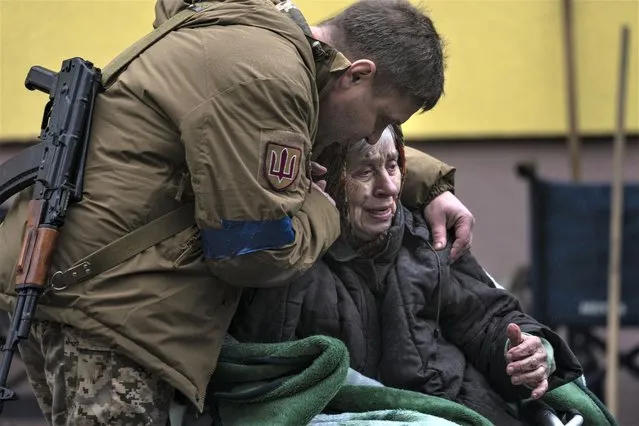 A soldier comforts Larysa Kolesnyk, 82, after being evacuated from Irpin, on the outskirts of Kyiv, Ukraine, Wednesday, March 30, 2022. (Photo by Rodrigo Abd/AP Photo)
