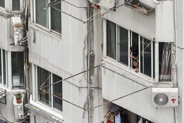 People look out the window of a residential building during a Covid-19 coronavirus lockdown in the Jing'an district in Shanghai on April 23, 2022. (Photo by Hector Retamal/AFP Photo)