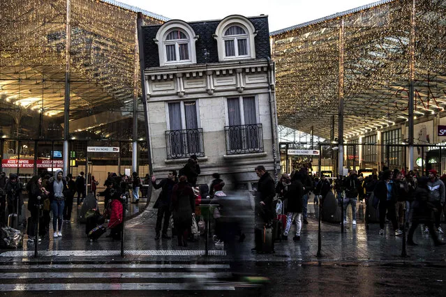 Commuters stand outside Gare du Nord train station and by the piece of art “Maison fond” (The melting house) by Argentinian artiste Leandro Erlich, in Paris on December 13, 2019, during a strike of Paris' public transports operator RATP and of the French state railway company SNCF employees over French government's plan to overhaul the country's retirement system. (Photo by Christophe Archambault/AFP Photo)