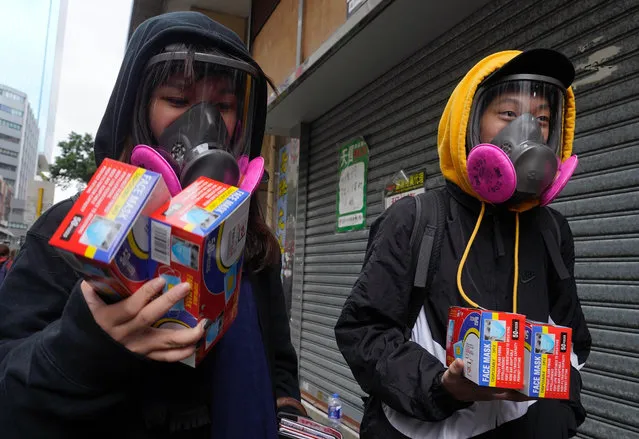 Citizens wearing full mask respirators carry packets of disposable face masks in Hong Kong, Wednesday, February 5, 2020. In Hong Kong, hospitals workers are striking to demand the border with mainland China be shut completely to ward off the virus, but four new cases without known travel to the mainland indicate the illness is spreading locally in the territory. (Photo by Vincent Yu/AP Photo)