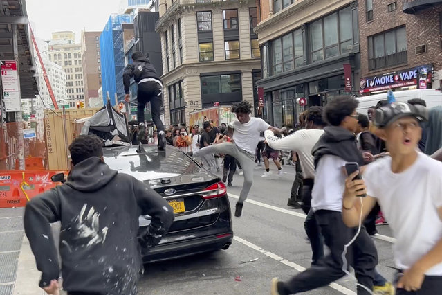 In this photo taken from video, people jump and kick a car as a crowd runs through the street on Broadway near Union Square, Friday, August 4, 2023, in New York. Police in New York City struggled to control a crowd of thousands of people who gathered in Manhattan's Union Square for an Internet personality's video game console giveaway that got out of hand. (Photo by Bobby Calvan/AP Photo)