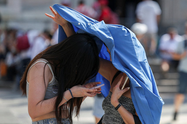 People use a piece of clothing to hide from the sun, during a heatwave in Milan, Italy on August 21, 2023. (Photo by Claudia Greco/Reuters)