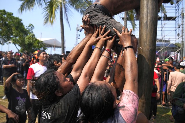 Participants assist a teammate during a greased-pole climbing competition held as a part of the Independence Day celebrations at Ancol Beach in Jakarta, Indonesia, Thursday, August 17, 2023. Indonesia is celebrating its 78th independence from the Dutch colonial rule. (Photo by Dita Alangkara/AP Photo)