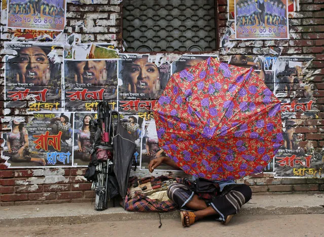 A Bangladeshi man fixes an umbrella as he sits in front of the posters of a film “Rana Plaza” pasted on the wall of a movie theatre in Dhaka, Bangladesh, Tuesday, August 25, 2015. Bangladesh's High Court has imposed a six-month ban on the screening of the movie about a garment worker who was rescued from the rubble 17 days after a five-story factory complex collapsed more than two years ago, killing more than 1,000 people. (Photo by A. M. Ahad/AP Photo)