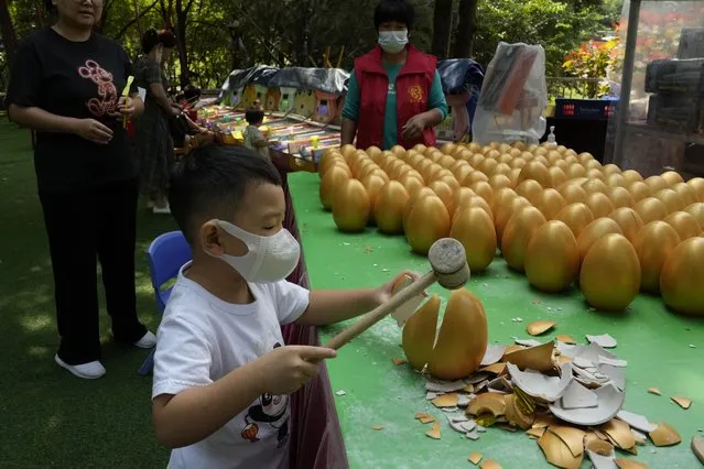 A child wearing a mask smashes a golden egg for a prize in Beijing, Monday, August 29, 2022. A Chinese think tank issued a rare public disagreement Monday with the ruling Communist Party's severe “zero COVID” policy, saying curbs that shut down cities and disrupt trade, travel and industry must change to prevent an “economic stall”. (Photo by Ng Han Guan/AP Photo)