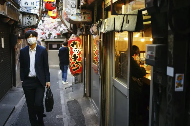 A man wearing a mask to help stop the spread of the new coronavirus walks along a bar alley in the Shinjuku Ward in Tokyo, Friday evening, April 24, 2020. Japan's Prime Minister Shinzo Abe expanded a state of emergency to all of Japan from just Tokyo and other urban areas as the virus continues to spread. (Photo by Eugene Hoshiko/AP Photo)