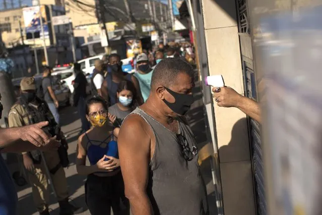 A man gets his temperature checked before entering the Madureira market amid the new coronavirus pandemic in Rio de Janeiro, Brazil, Wednesday, June 17, 2020. Rio continues with its plan to ease restrictive measures and open the economy to avoid an even worse economic crisis. (Photo by Silvia Izquierdo/AP Photo)