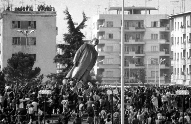 Hundreds of Albanians push over the bronze statue of the late communist dictator Enver Hoxha located in the central square of Tirana, February 20, 1991. Thousand others cheer from the roofs of the buildings as the last symbol of the communist dictatorship is forcefully removed. A rally was organised February 20 by the opposition to commemorate the 9th anniversary when Albanians toppled the statue of the late communist dictator Enver Hoxha from Tirana's central square. (Photo by Lulzim Lika/Reuters)