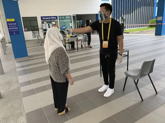 A voter, left, wearing a face mask has her temperature checked with a thermal scanner at the Dunearn Secondary School polling station in Singapore Friday, July 10, 2020. Wearing masks and plastic gloves, Singaporeans began voting in a general election that is expected to return Prime Minister Lee Hsien Loong's long-ruling party to power. (Photo by Royston Chan/AP Photo)
