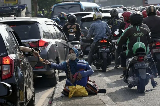 A motorist gives money to beggars while stuck in the morning rush hour traffic in Jakarta, Indonesia, Monday, November 14, 2022. The 8 billionth baby on Earth is about to be born on a planet that is getting hotter. But experts in climate science and population both say the two issues aren't quite as connected as they seem. (Photo by Tatan Syuflana/AP Photo)