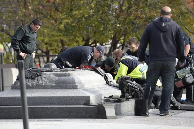 Emergency personnel tend to a soldier shot at the National Memorial near Parliament Hill in Ottawa on Wednesday October 22, 2014. The soldier was standing guard when an unknown gunman shot him. The gunman reportedly ran towards Parliament Hill, which is currently under lockdown and surrounded by security.  Prime Minister Stephen Harper was rushed away from the building to an undisclosed location, officials in his office said. (Photo by Adrian Wyld/AP Photo/The Canadian Press)