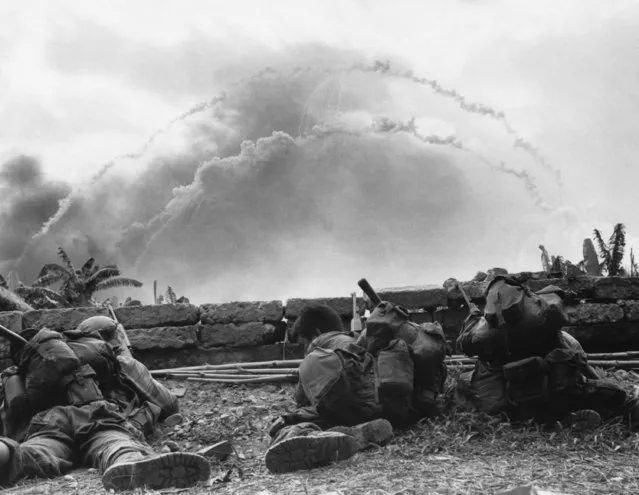 Three Vietnamese Special Forces troopers take cover behind a low wall while white phosphorous grenades being fired make a rainbow shaped are through the sky in the background. The soldiers from the mobile strike force (Mike) are engaging North Vietnamese troopers who overrun outposts near the Thuong Duc Special Forces camp, 30 miles West Southwest of Danang, September 30, 1968. (Phoot by AP Photo/Phuoc)