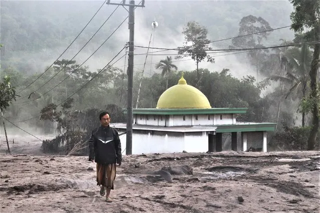 A man walks past a mosque partially covered in volcanic ash from the eruption of Mount Semeru in Kajar Kuning village in Lumajang, East Java, Indonesia, Monday, December 5, 2022. (Photo by Imanuel Yoga/AP Photo)