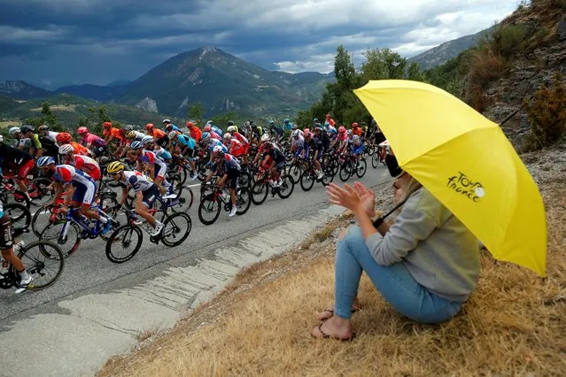 A woman carries a yellow umbrella with the Tour de France logo as the peloton passes by Nice to Sisteron, France on August 31, 2020. (Photo by Stephane Mahe/Reuters)