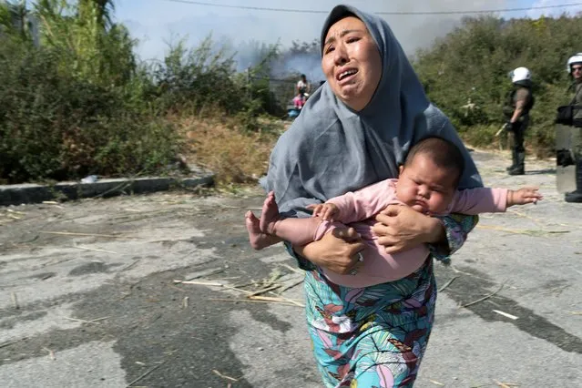 A migrant holds her baby as she runs to avoid a small fire in a field near Mytilene town, on the northeastern island of Lesbos, Greece, Saturday, September 12, 2020. Thousands of asylum-seekers spent a fourth night sleeping in the open on the Greek island of Lesbos, after successive fires destroyed the notoriously overcrowded Moria camp during a coronavirus lockdown. (Photo by Petros Giannakouris/AP Photo)