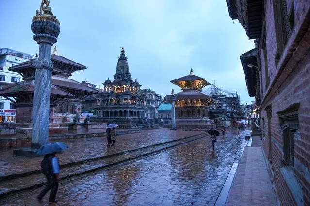 Residents carrying umbrellas walk on an almost deserted Durbar Square under the rain after restrictions were imposed by district officials for a week to contain the spread of the COVID-19 coronavirus, in Patan (Lalitpur) on the outskirts of Kathmandu on August 26, 2020. (Photo by Prakash Mathema/AFP Photo)