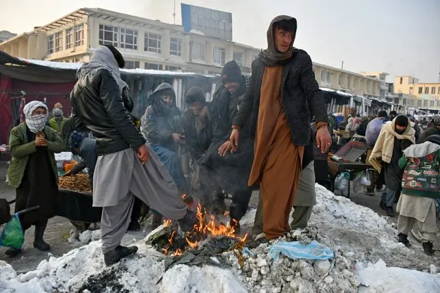 In this photograph taken on January 14, 2023, Afghan men warm themselves around a bonfire at a market in Mazar-i-Sharif. (Photo by Atif Aryan/AFP Photo)