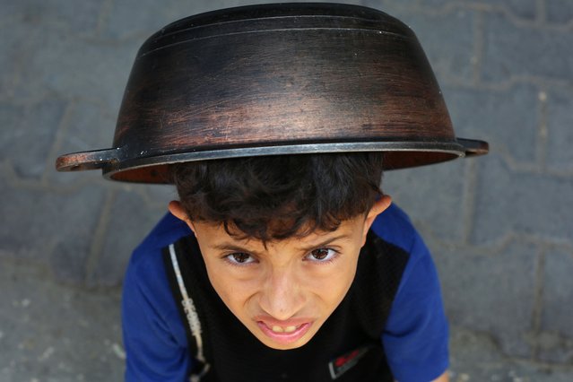 A Palestinian boy waits next to a queue at a food distribution point in Nuseirat, in the central Gaza Strip, on June 23, 2025. The Israeli blockade imposed in early March amid an impasse in truce negotiations had produced famine-like conditions across Gaza, according to rights groups. (Photo by Eyad Baba/AFP Photo)