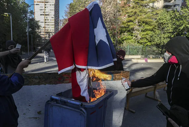 Demonstrators burn a Chilean flag during a protest against police in reaction to a video that appears to show an officer pushing a youth off a bridge the previous day at a protest, in Santiago, Chile, Saturday, October 3, 2020. (Photo by Esteban Felix/AP Photo)