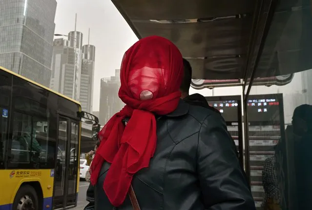 A woman wears a mask and scarf over her face as she waits for a bus during a sandstorm on April 11, 2023 in Beijing, China. (Photo by Kevin Frayer/Getty Images)