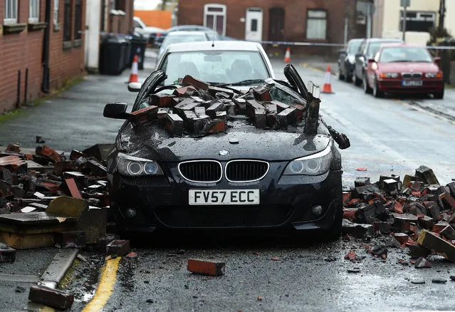 A parked car is crushed by masonry after high winds forced the gable end of an apartment block to collapse in Leigh, north west England on November 18, 2015. The building was evacuated in the early hours of the morning as a storm, named "Barney" by meteorological authorities sweeps across Britain. (Photo by Paul Ellis/AFP Photo)