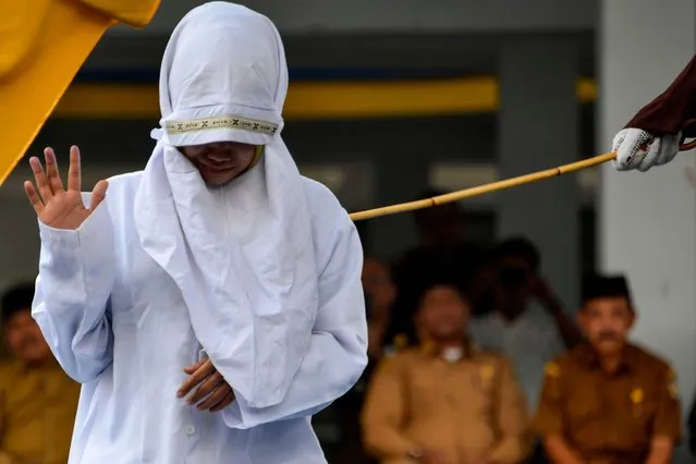 A woman reacts as she is caned in public by a member of the Sharia police in Banda Aceh on March 2, 2020. Aceh is the only region in the world's biggest Muslim-majority nation that imposes Islamic law – known as Sharia – with those found guilty of breaches often publicly whipped with a rattan cane. (Photo by Chaideer Mahyuddin/AFP Photo)