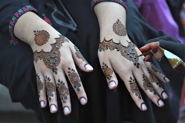 A beautician paints hands of customers with traditional henna in preparation for the upcoming Eid al-Fitr celebrations, in Karachi, Pakistan, Thursday, April 20, 2023. Eid al-Fitr marks the end of the Islamic holy month of Ramadan. (Photo by Fareed Khan/AP Photo)