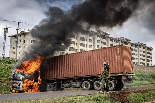 A Kenyan police officer calls for reinforcement in front of a lorry set on fire by protesters during riots in the informal settlement of Kibera in Nairobia on May 2, 2023. Kenyan riot police were out on the streets on May 2, 2023 as the opposition defied a police ban and staged new demonstrations over the cost of living crisis and last year's election results. (Photo by Luis Tato/AFP Photo)