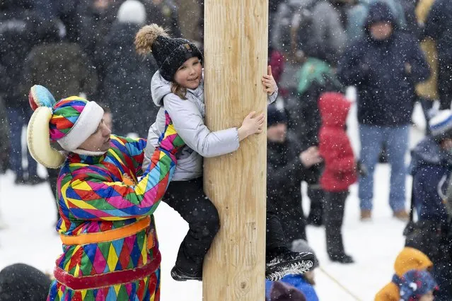 An actor wearing a costume of a Russian parsley (clown) helps a girl to climb up a wooden pole to get a prize during during Maslenitsa (Shrovetide) holiday celebrations at the Izmailovsky Kremlin in Moscow, Russia, Saturday, March 13, 2021. Maslenitsa is an Orthodox Christian holiday celebrated in the last week before the Orthodox Lent. The festivities feature baking traditional pancakes, sleigh rides, sparring between groups of men and, finally burning the effigy of Maslenitsa. (Photo by Alexander Zemlianichenko/AP Photo)