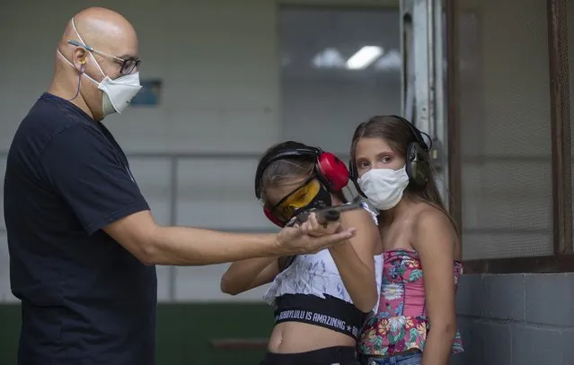 Instructor Robson de Oliveira trains his 10-year-old twin daughters Lorena, center, and Lara, how to properly shoot a firearm at a shooting range in Americana, in the Sao Paulo state of Brazil, Saturday, March 6, 2021. As authorized by two of the most divisive presidential decrees, average Brazilians will be able to own six guns, up from four currently, and carry two simultaneously. (Photo by Andre Penner/AP Photo)