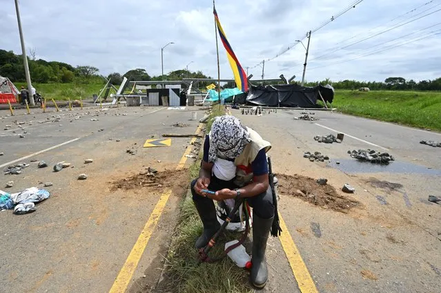 An indigenous demonstrator looks at his mobile phone near a barricade blocking the Panamerican highway during a protest against the government triggered by a now abandoned tax reform bill, in Cali, Colombia, on May 10, 2021. Indigenous and other demonstrators announced Monday the temporary reopening of highways in southwestern Colombia, which had been blocked in the framework of massive protests against the government taking place in the last 13 days, and which have left 27 dead. (Photo by Luis Robayo/AFP Photo)