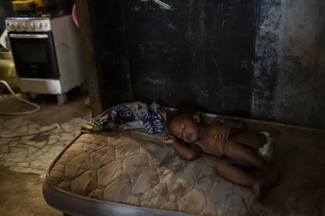 Ana Beatriz sleeps on a mattress while her mother Debora Estanislau, who before the new coronavirus pandemic hit made a living as a domestic worker cooks, in the house where she lives with her four children at the Cidade de Deus favela, in Rio de Janeiro, Brazil, Sunday, April 18, 2021. (Photo by Bruna Prado/AP Photo)