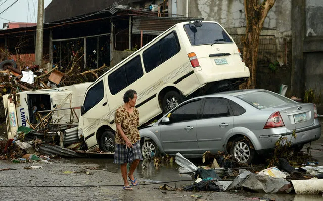 A woman walks past stacked up vehicles in Tacloban, eastern island of Leyte in November 12, 2013. (Photo by Noel Celis/AFP Photo)