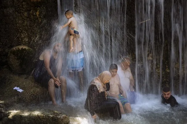 Israeli Arabs stand under a waterfall during the Muslim Eid al-Adha holiday at the Gan HaShlosha national park near the northern Israeli town of Beit Shean, Wednesday, July 21, 2021. Eid al-Adha meaning “Feast of Sacrifice”, this most important Islamic holiday marks the willingness of the Prophet Ibrahim (Abraham to Christians and Jews) to sacrifice his son. During the holiday, which in most places lasts four days, Muslims slaughter sheep or cattle, distribute part of the meat to the poor. (Photo by Oded Balilty/AP Photo)