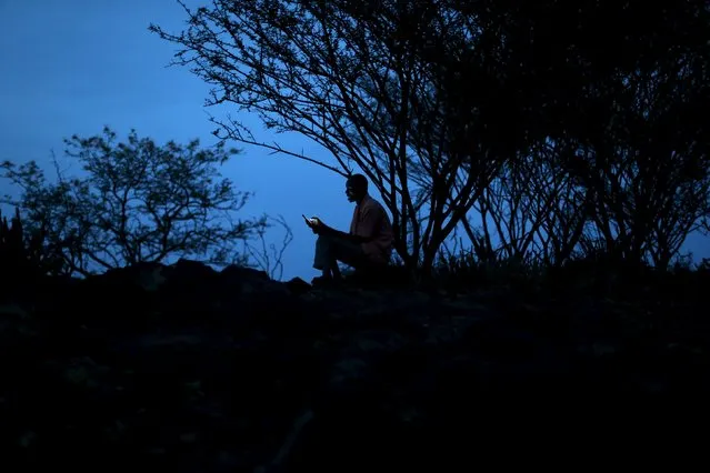 A man sits on top of a hill at dusk as he searches for network on his mobile phone the day before an initiation ceremony for young men in Baringo County, Kenya, January 19, 2016. (Photo by Siegfried Modola/Reuters)