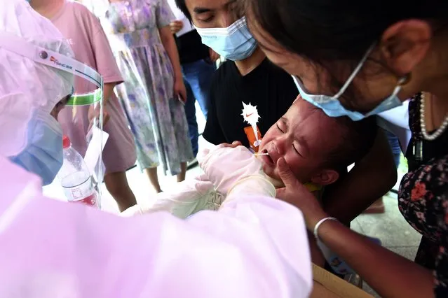 A medical worker takes swab samples from a chid during mass testing for COVID-19 at a residential block in Wuhan in central China's Hubei province Tuesday, August 3, 2021. China suspended flights and trains, canceled professional basketball league games and announced mass coronavirus testing in Wuhan on Tuesday as widening outbreaks of the delta variant reached the city where the disease was first detected in late 2019. (Photo by Chinatopix via AP Photo)